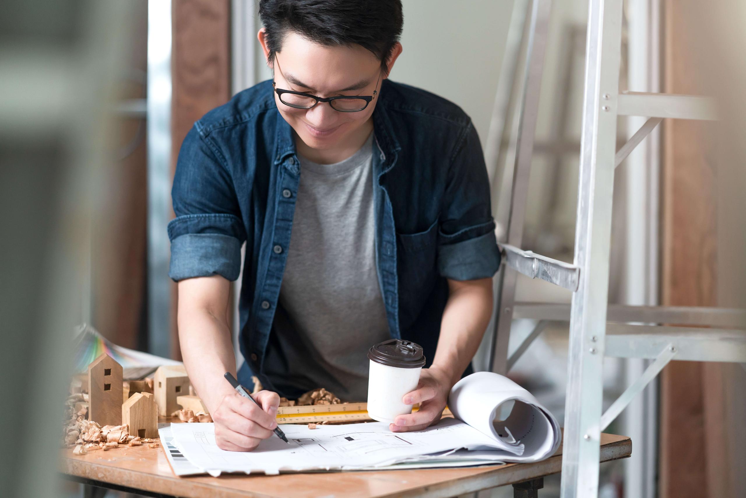 asian attractive glasses interior designer working at house site renovation construction progress with smile and confident at desk with blue print and drawing tool